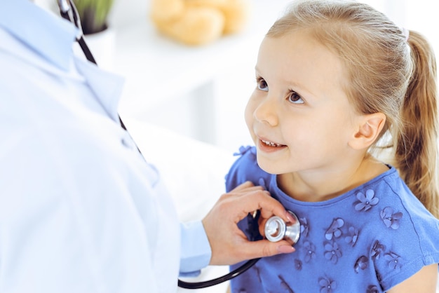 Médico examinando uma garotinha pelo estetoscópio. Paciente criança sorridente feliz na inspeção médica habitual. Conceitos de medicina e saúde.
