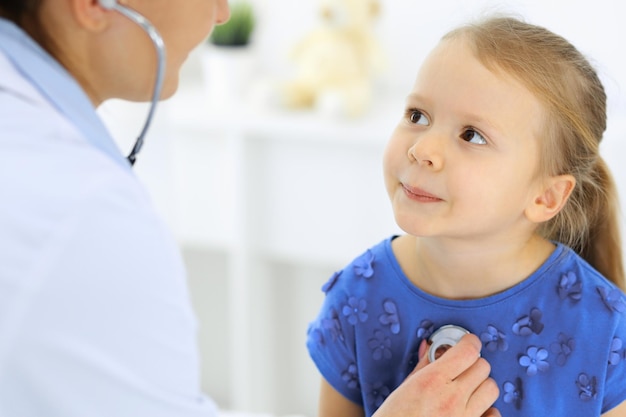 Médico examinando uma garotinha pelo estetoscópio. paciente criança sorridente feliz na inspeção médica habitual. conceitos de medicina e saúde.