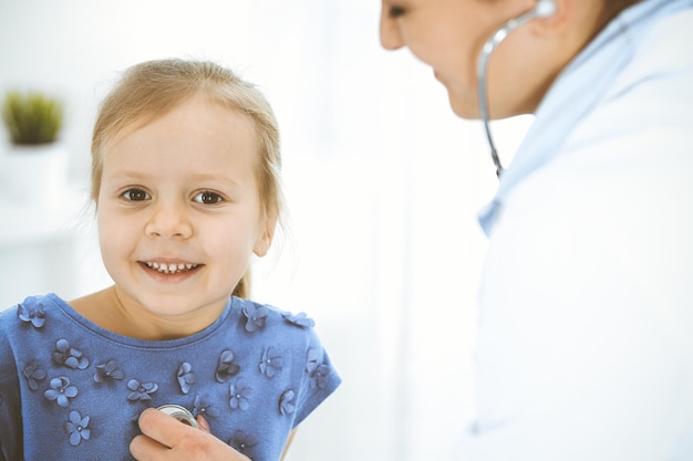 Médico examinando uma garotinha pelo estetoscópio paciente criança sorridente feliz na inspeção médica habitual conceitos de medicina e saúde