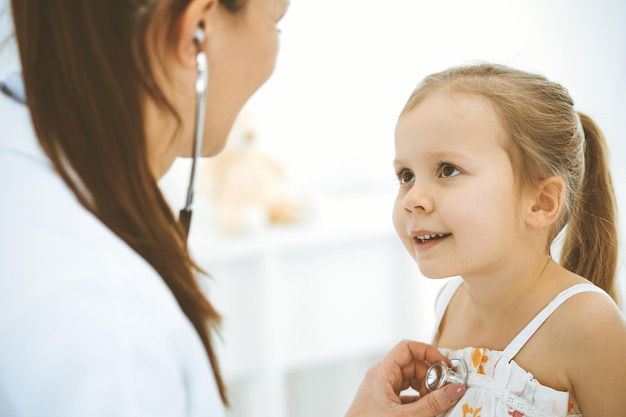 Médico examinando uma garotinha pelo estetoscópio Paciente criança sorridente feliz na inspeção médica habitual Conceitos de medicina e saúde