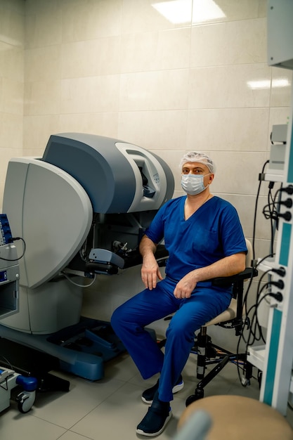 Médico experiente senta-se na cadeira perto do equipamento de controle para fornecer operação à distância com a ajuda da máquina robótica closeup