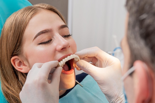 médico experimenta uma dentadura nos dentes superiores para um paciente sentado em uma cadeira