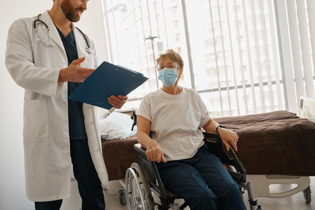 Médico explicando a um paciente doente em cadeira de rodas os detalhes do tratamento