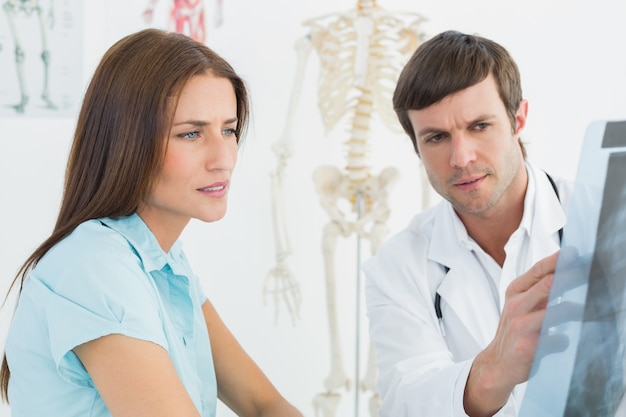 Médico explicando radiografía de columna a paciente femenino