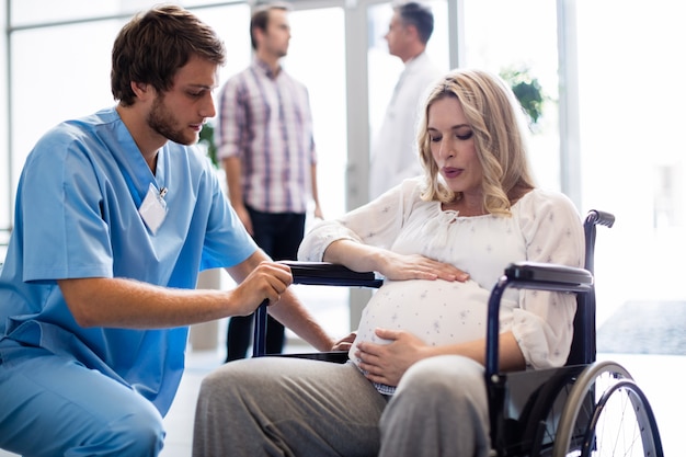 Médico falando com mulher grávida em cadeira de rodas
