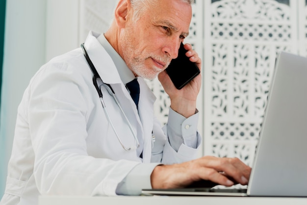 Foto médico falando no telefone e usando o laptop