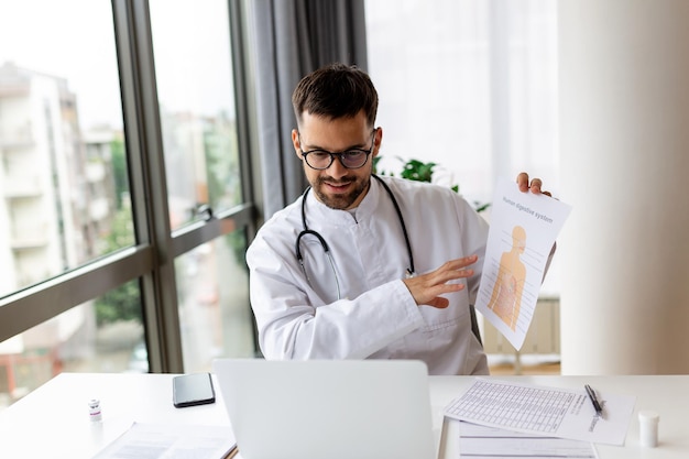 Médico falando online com paciente mostrando-lhe o sistema digestivo na área de transferência fazendo videochamada