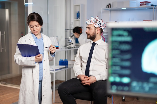 Médico falando sobre os sintomas da doença durante as investigações usando fone de ouvido de varredura de ondas cerebrais de alta tecnologia. pesquisador analisando o estado de saúde do paciente homem, funções cerebrais, sistema nervoso.