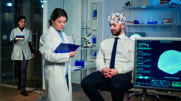 Médico falando sobre sintomas de doenças durante investigações usando fones de ouvido de alta tecnologia para varredura de ondas cerebrais