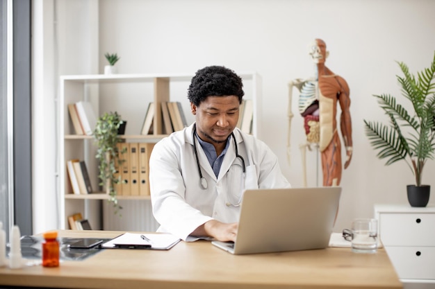 Médico de familia que trabaja en la computadora portátil en la oficina de la clínica médica