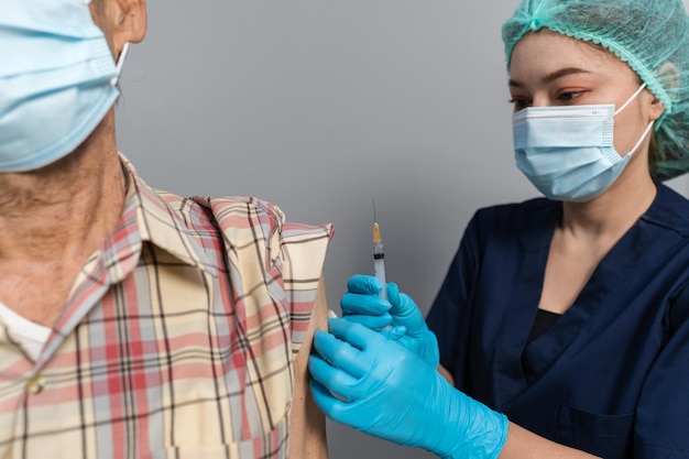Médico faz injeção Covid19 ou vacina coronavírus para paciente sênior com máscara médica