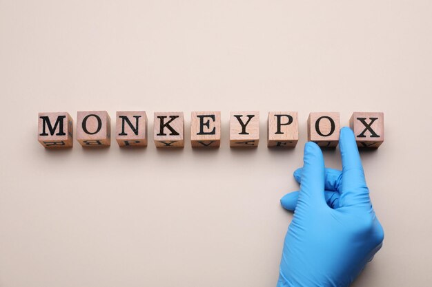 Médico fazendo palavra Monkeypox com cubos de madeira na vista superior de fundo bege
