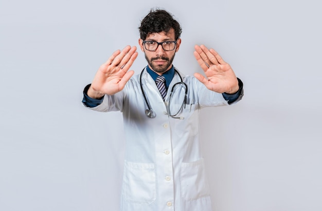 Médico fazendo um gesto de parada com as palmas das mãos em fundo isolado Jovem médico fazendo um gesto de parada com as mãos isoladas