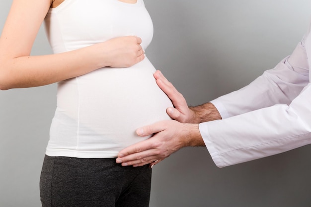 Médico feliz se preocupando com o médico da jovem grávida usando a mão examinando a mulher grávida na clínica