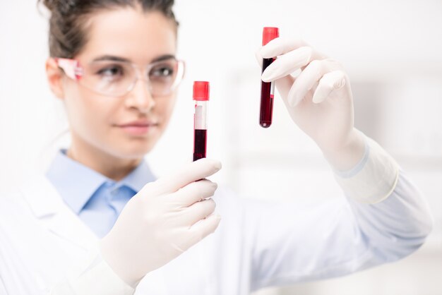 Médico femenino contemporáneo en guantes con muestras de nueva vacuna desarrollada en laboratorio médico