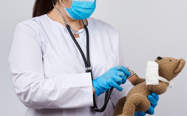 Médico femenino tiene oso de peluche marrón con la pata vendada en vendaje blanco