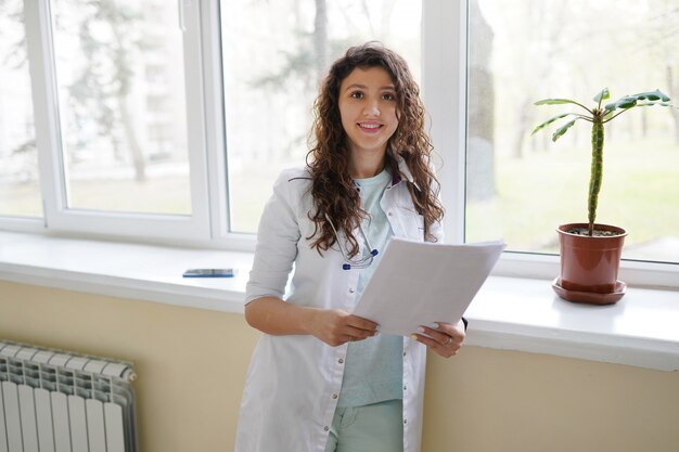 Médico feminino atraente usando um estetoscópio, olhando para a câmera com um sorriso