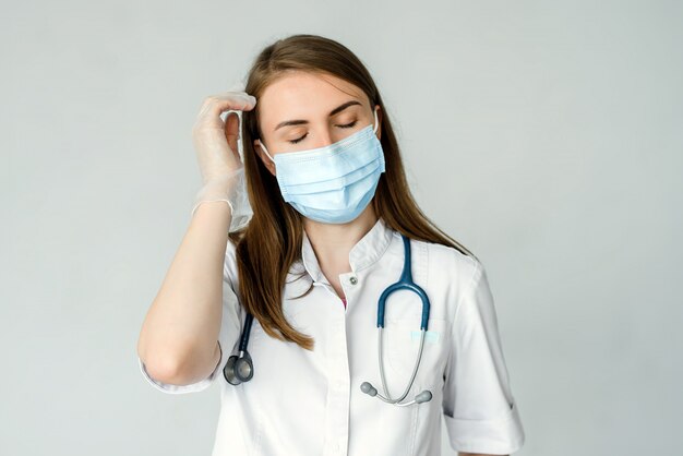 Médico feminino cansado na máscara médica e boné tem uma dor de cabeça isolada sobre cinza