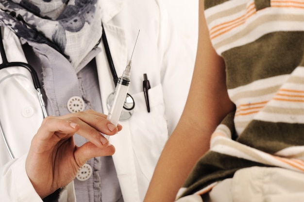 Médico feminino muçulmano no hospital dando uma injeção para um menino