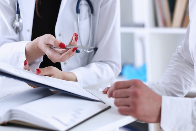 Médico feminino segurando uma caneta prateada e mostrando um bloco