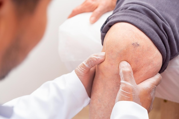 Médico fisioterapeuta examinando, massageando e tratando o joelho e a perna do paciente idoso no hospital de enfermagem da clínica médica ortopédica.