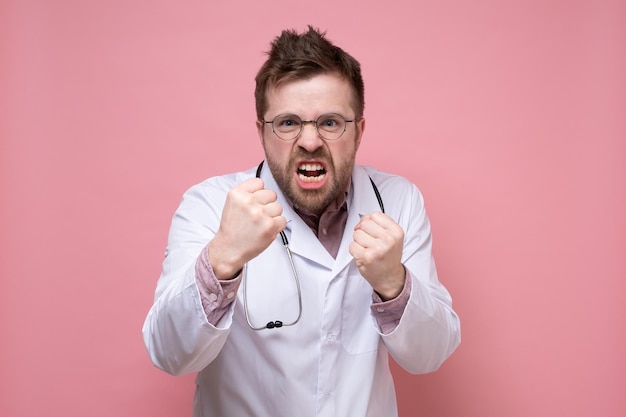 El médico furioso con un estetoscopio alrededor del cuello mantiene los puños y está listo para pelear, parece loco