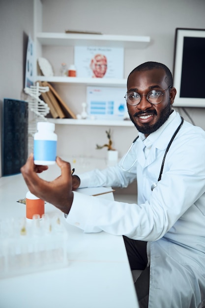 Médico general multiétnico levantando un frasco de pastillas azul