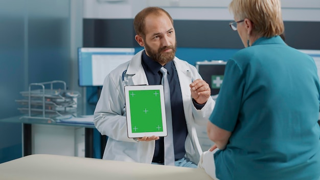 Médico general que usa tableta digital con pantalla verde en el examen médico con el paciente. Doctor sosteniendo fondo de maqueta aislado con plantilla de clave de croma y espacio de copia en blanco.