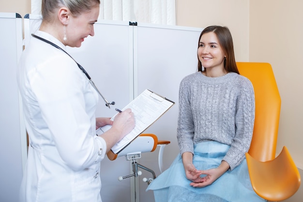 Médico ginecologista conversando com uma paciente em uma cadeira laranja em um consultório médico