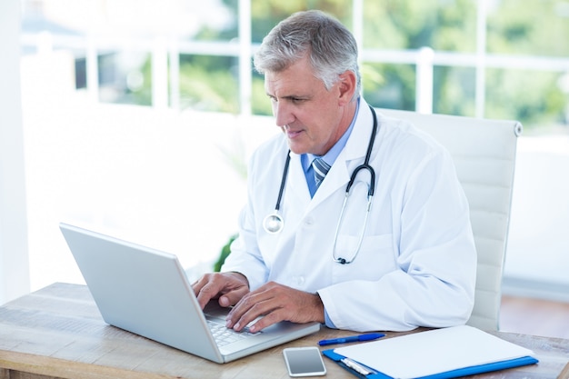 Foto médico grave trabalhando no laptop em sua mesa