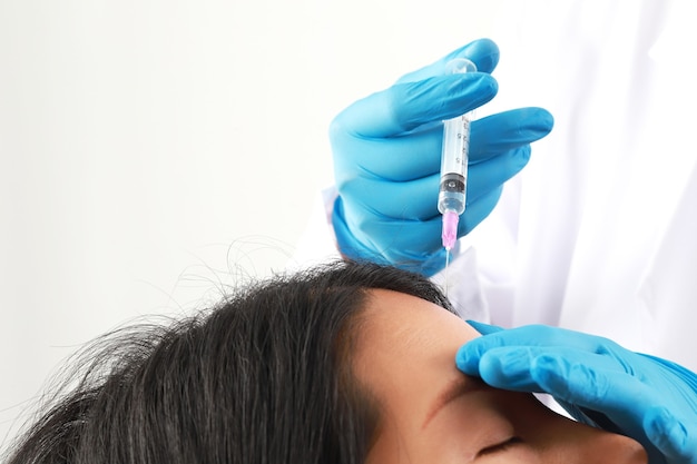 Un médico con guantes azules inyecta a una mujer en la frente para realzar su belleza.