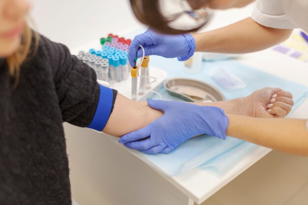 Foto un médico con guantes azules toma sangre de una vena de una mujer joven. varios tubos de ensayo. diagnóstico, enfermedad, concepto de examen.