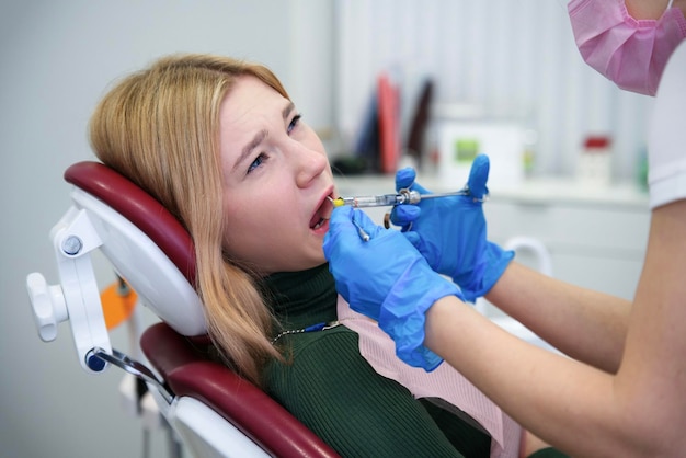 El médico con guantes y máscara médica inyecta una inyección de analgésico anestesia dentista examinando