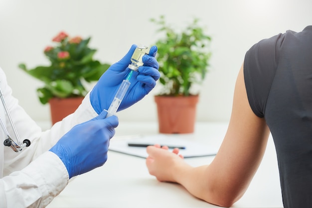 Un médico con guantes médicos desechables que extrae una vacuna de una botella con una jeringa