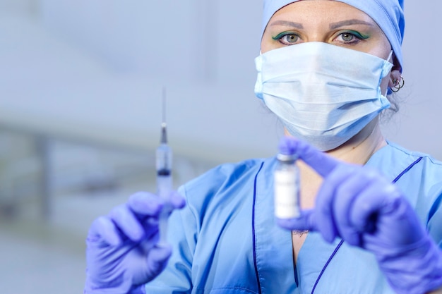 Un médico con guantes médicos y una máscara sostiene un vial con una vacuna y una jeringa. Foto horizontal