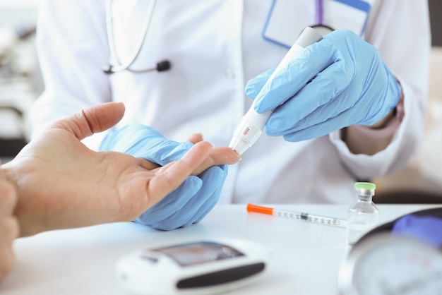 Médico con guantes perforando el dedo del paciente con primer plano de lanceta. Monitoreo de glucosa en sangre