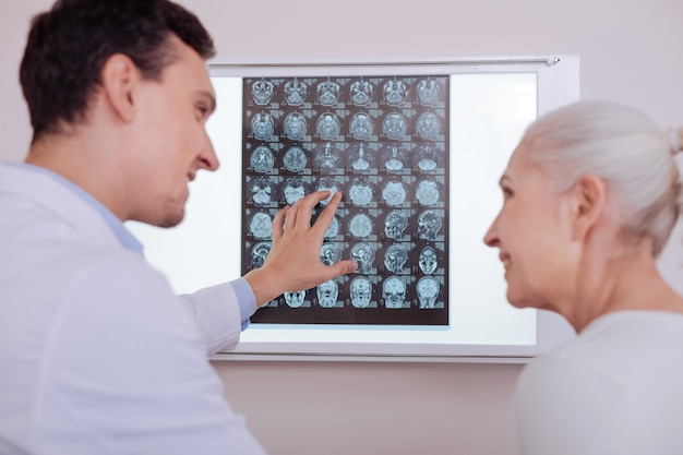 Foto médico guapo positivo encantado mirando a su paciente y sonriendo mientras le dice buenas noticias