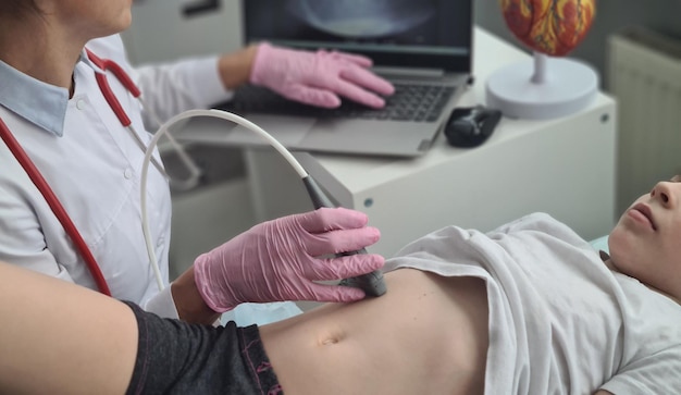 El médico hace una ecografía de la cavidad abdominal para una niña usando un escáner en la clínica