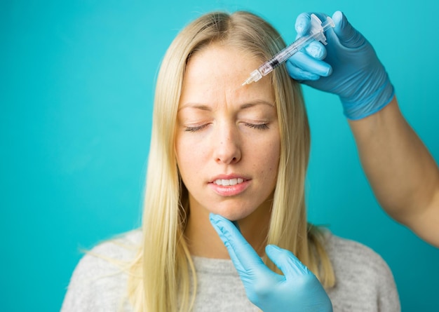 El médico hace las inyecciones faciales rejuvenecedoras para suavizar la piel de la cara de una mujer joven