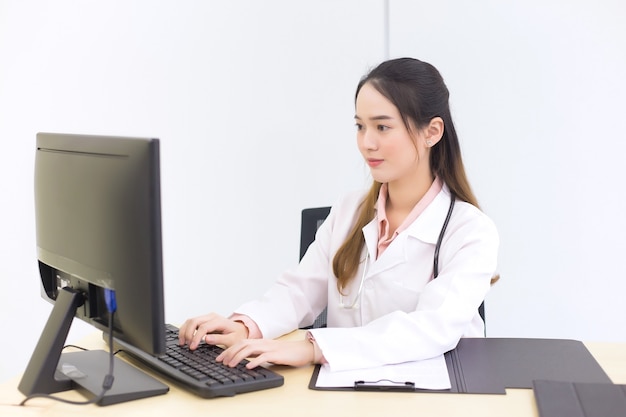 Médico de la hermosa mujer asiática está escribiendo en un teclado para guardar información en la computadora