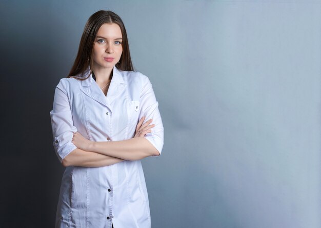 Médico de la hermosa niña en una bata médica blanca sobre un fondo gris