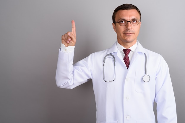 Médico hombre con anteojos contra la pared gris