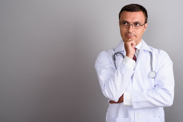 Médico hombre con anteojos contra la pared gris