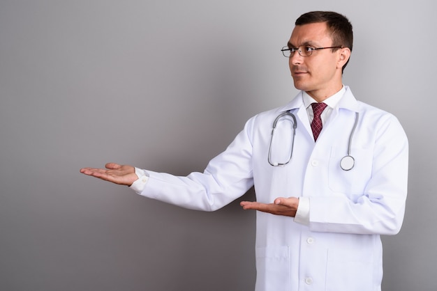 Médico hombre con anteojos contra la pared gris