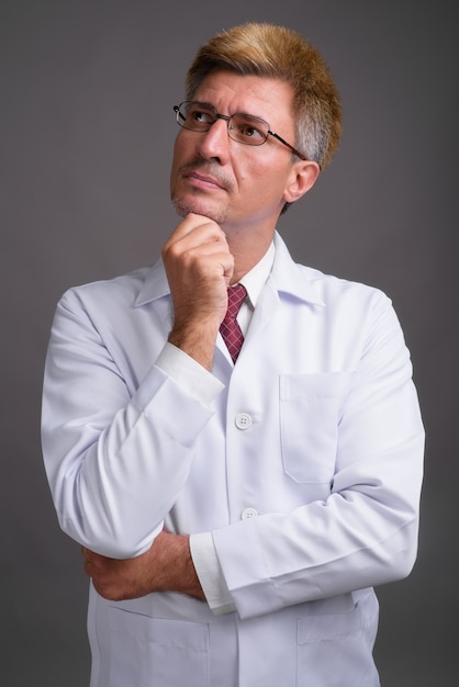 Médico hombre con cabello rubio contra la pared gris