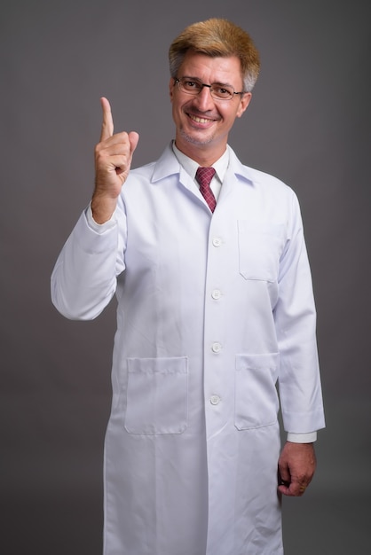 Médico hombre con cabello rubio contra la pared gris