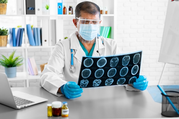 Médico hombre examinando la cabeza por resonancia magnética mientras está sentado en la mesa en el hospital