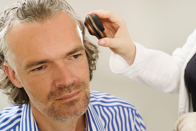 Foto médico y hombre de mediana edad en la clínica de dermatología el dermatólogo está usando un dermatoscopio para el examen de la piel facial