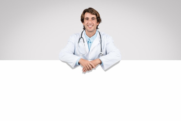 Un médico hombre sonriente apoyándose en un anuncio médico de bandera blanca