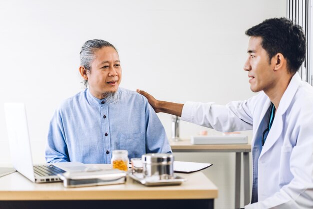 Médico homem asiático vestindo uniforme com estetoscópio ajuda a discutir e segurando paciente homem sênior asiático, tranquilizando-o com cuidados de confiança em hospital.